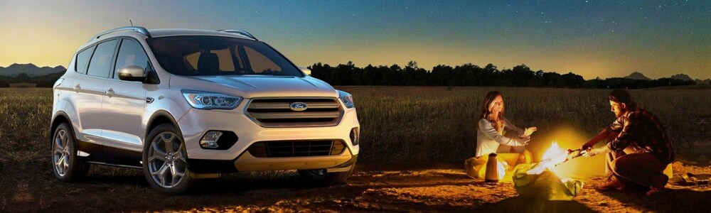 2019 Ford Escape models in Raton NM at Phil Long Ford of Raton.png A young couple sitting by a campfire at dusk with their brand new white 2019 Ford Escape SUV parked beside them