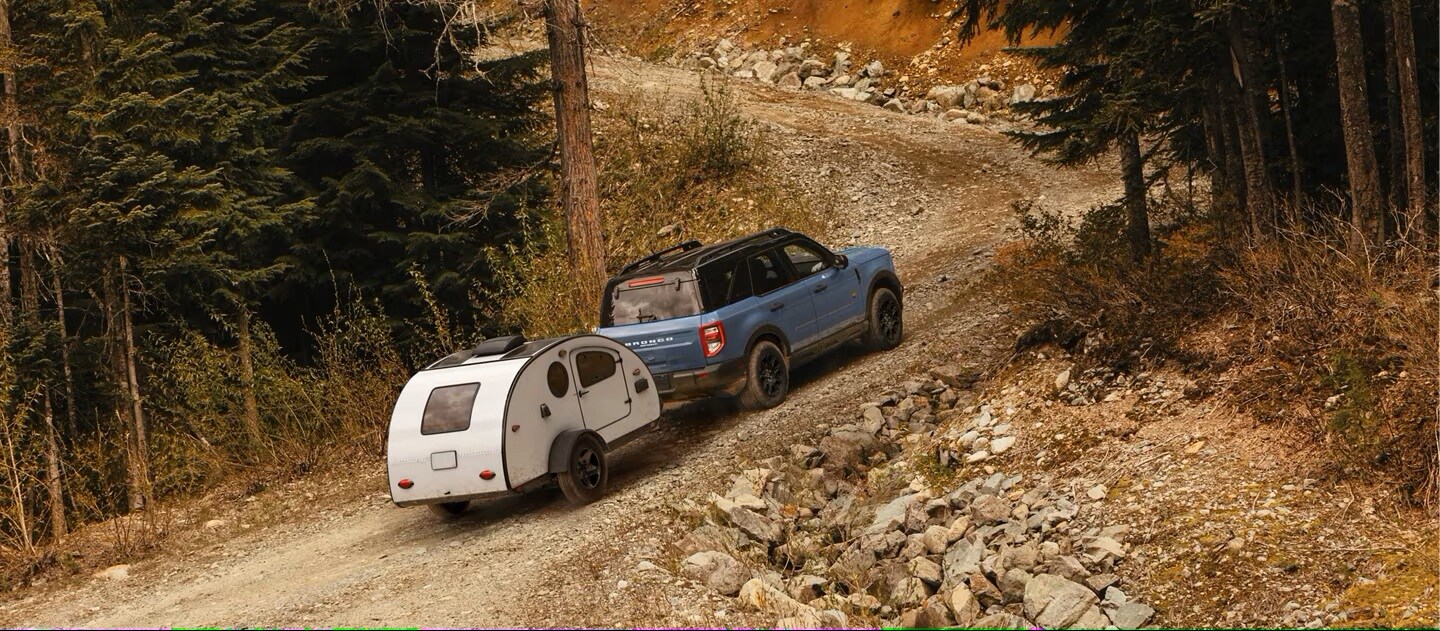 A Ford Bronco Sport hauling a small trailer up a dirt mountain road.