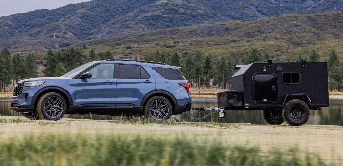 2025%20Ford%20Explorer.4.jpg A Metallic Blue 2025 Ford Explorer towing a camping with a lake and a mountain in the background.