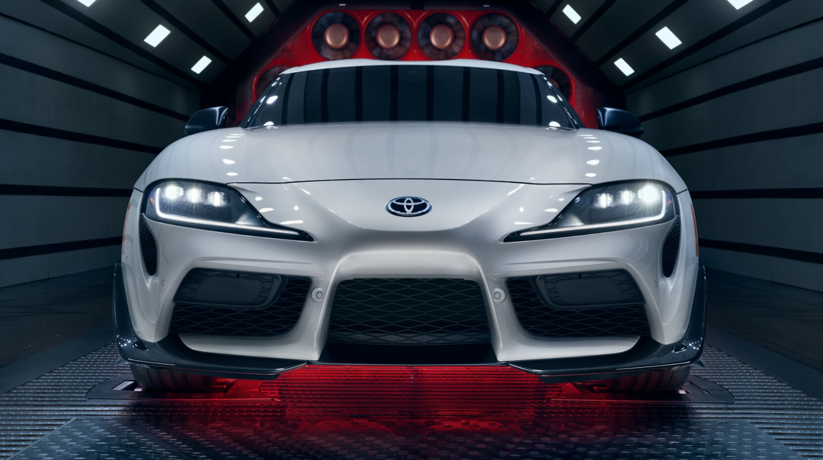 2022-Toyota-Supra-2.PNG a Supra parked in a small custom metallic garage with red lights are emanating behind the new car