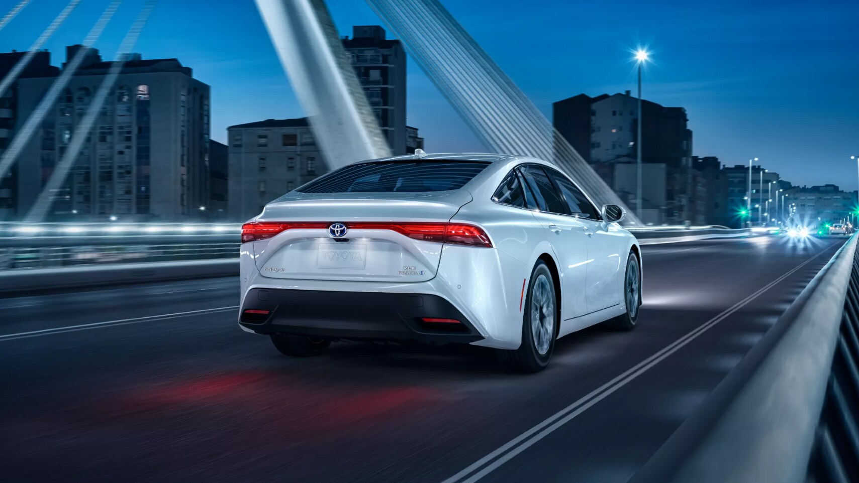 2022-Toyota-Mirai-2.PNG A view of the back of a white 2022 toyota Mirai as it drives away from the viewer across a bridge