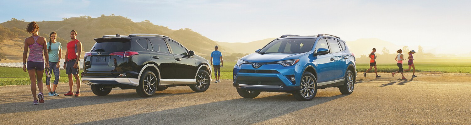 New 2019 Toyota RAV4 for sale in Colorado at Phil Long Toyota Trinidad.png Lifestyle photograph of two 2019 Toyota Rav4 models parked on a dirt opening as the sun rises in the background with drivers and passengers getting ready to exercise