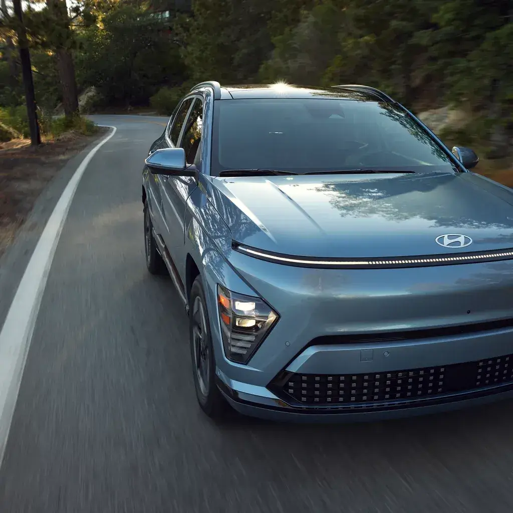 Blue Hyundai Kona Electric driving on a forest road, front view