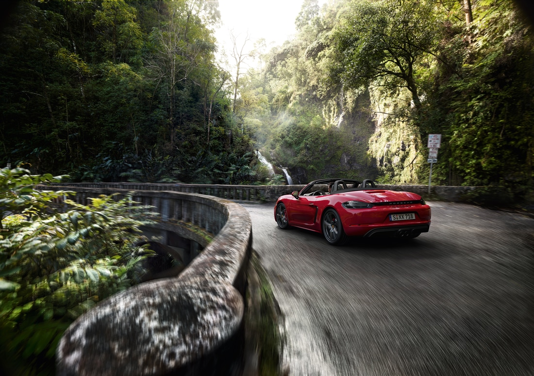 2022-Porsche-718-BoxsterGTS-Convertible-L04.png red Porsche 718 Boxster GTS convertible driving across an old stone bridge, surrounded by tropical greenery