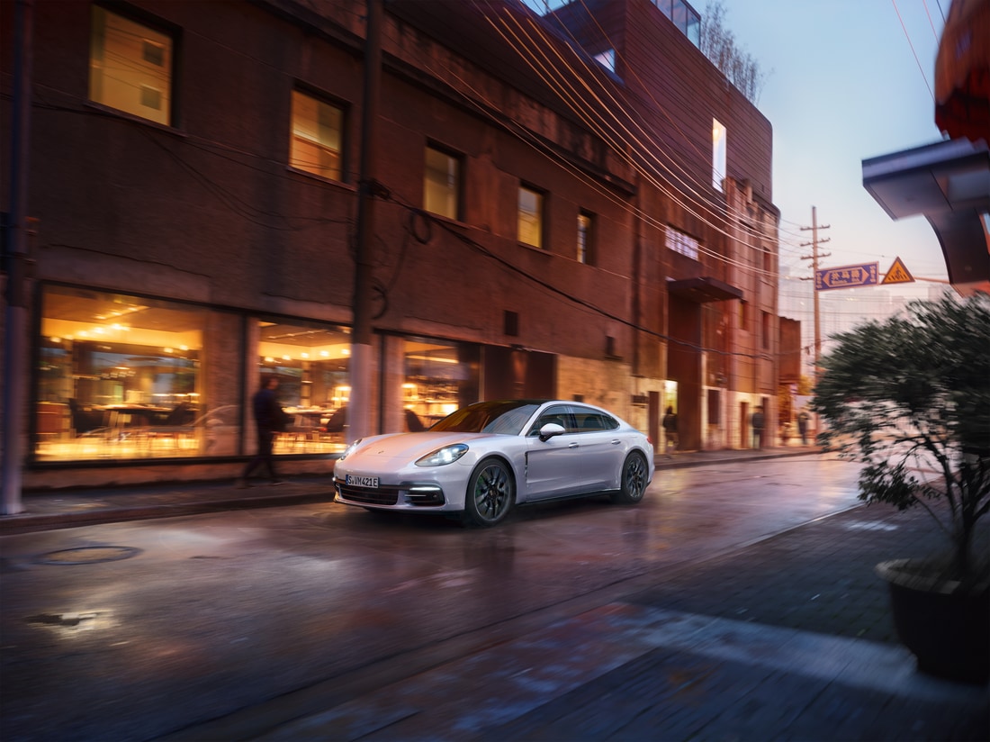 2022-Porsche-Panamera-4EHybrid-Base-Hatchback-L01.png white Porsche Panamera Hybrid driving through a brick-lined downtown street