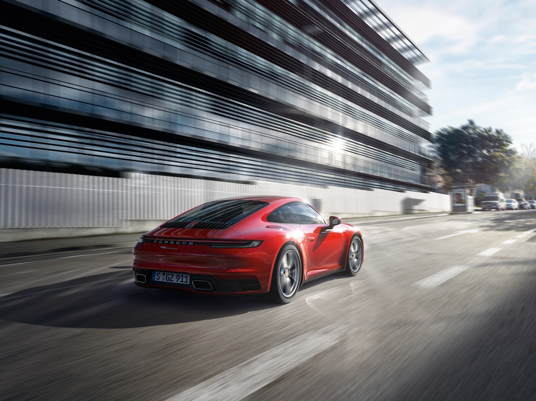 red Porsche 911 Carrera driving fast past a glass building