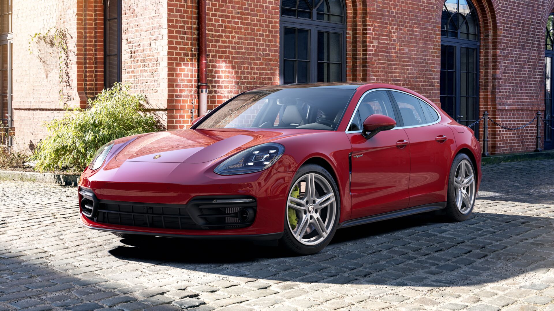 red Porsche Panamera sports car parked on a cobblestone street in front of a brick building