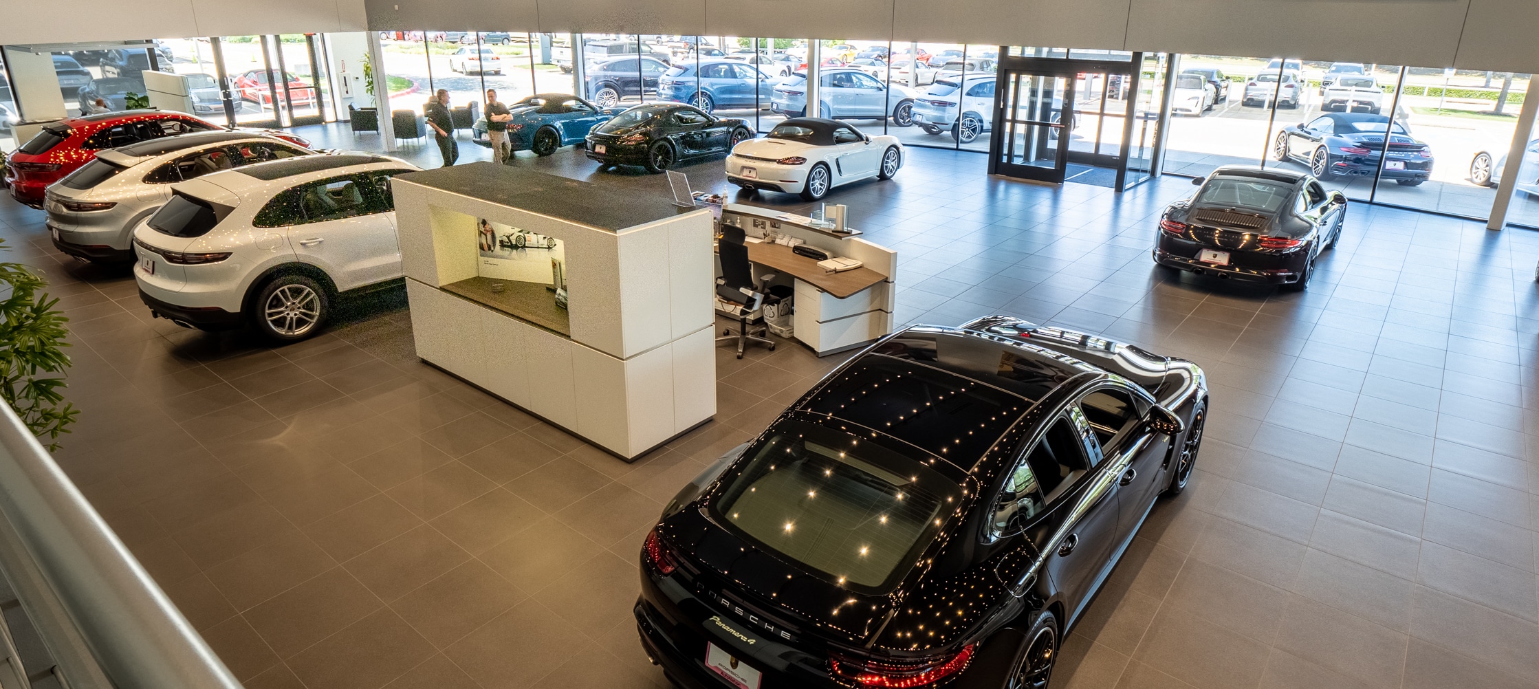 Find out about financing at Porsche Plano Interior view of Porsche Plano with an overhead view of several Porsche vehicles parked inside the lobby