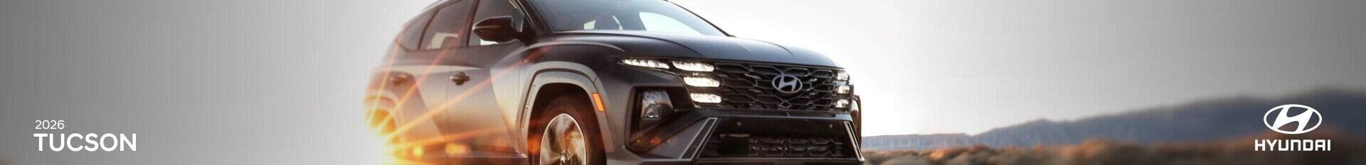Front three-quarter view action shot of a dark gray 2026 Hyundai Tucson driving down a sunny highway.