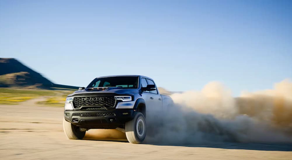 A silver 2025 Ram 1500 RHO is off-roading on a sandy area.