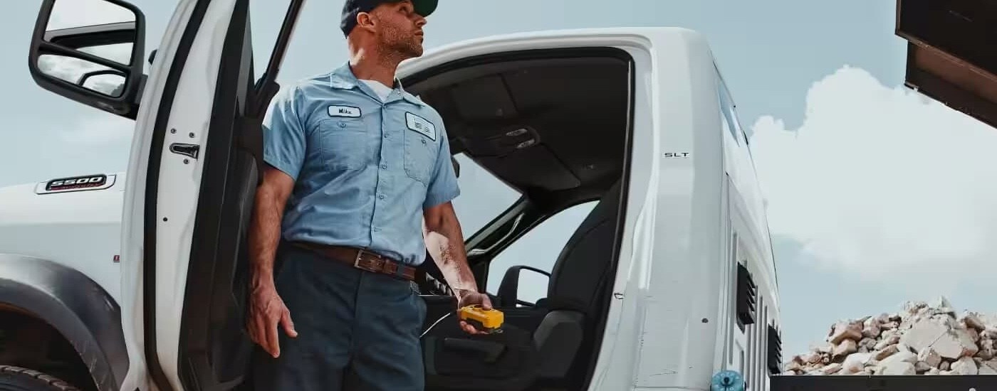 A man is standing next to the open door of a white 2024 Ram 5500.