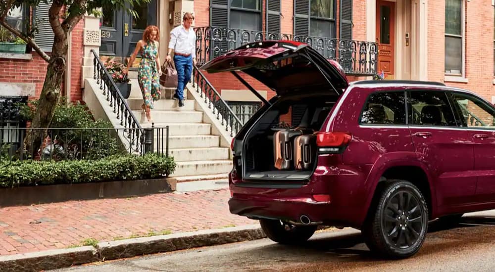 A red 2022 Jeep Grand Cherokee WK is parked on the side of a street with the rear storage door open.