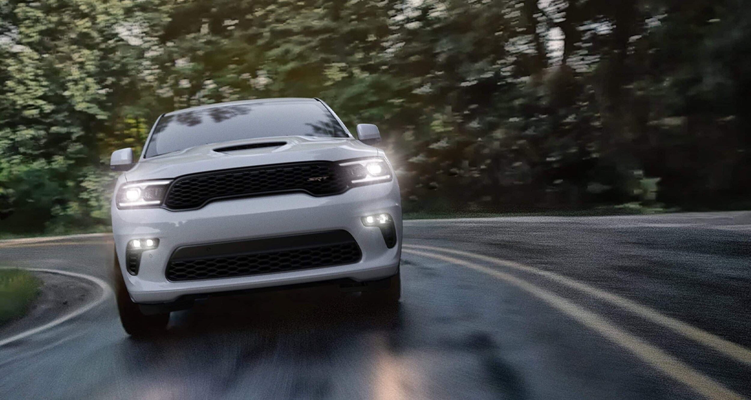 A white 2022 Dodge Durango SRT is driving on a winding road after shopping for a used Dodge for sale.
