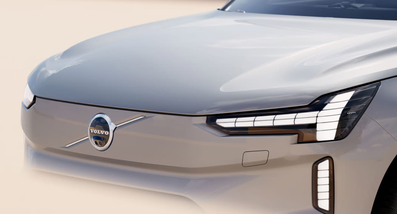 Close-up of a sleek silver Volvo EX90 front, featuring a prominent Volvo logo, modern headlight design, and smooth curves.