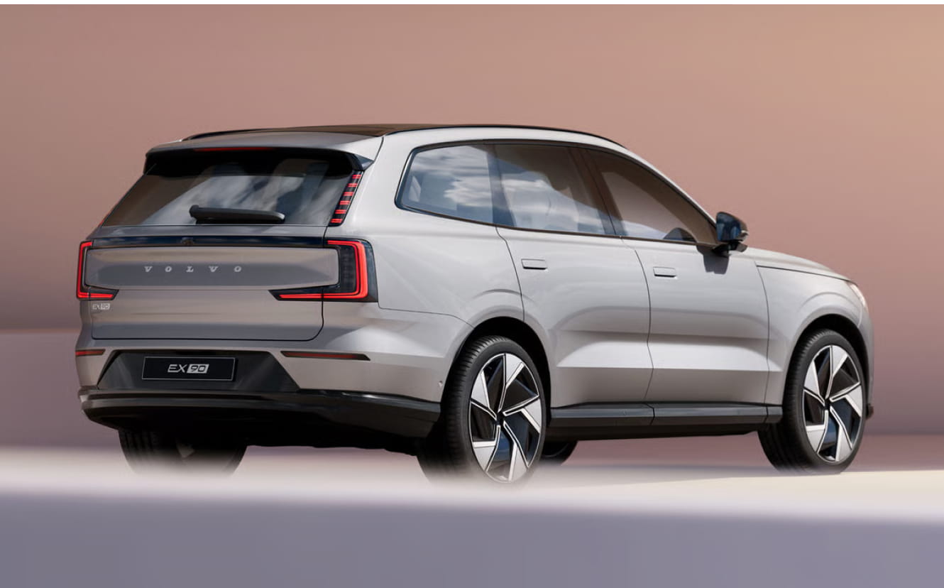 Volvo EX90 SUV is displayed from a rear side angle against a gradient pinkish background.