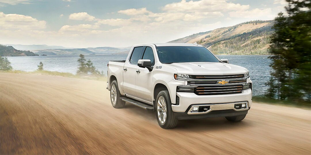 vue trois quart avant du Chevrolet Silverado 1500 2021 roulant sur un sentier proche d'une étendue d'eau