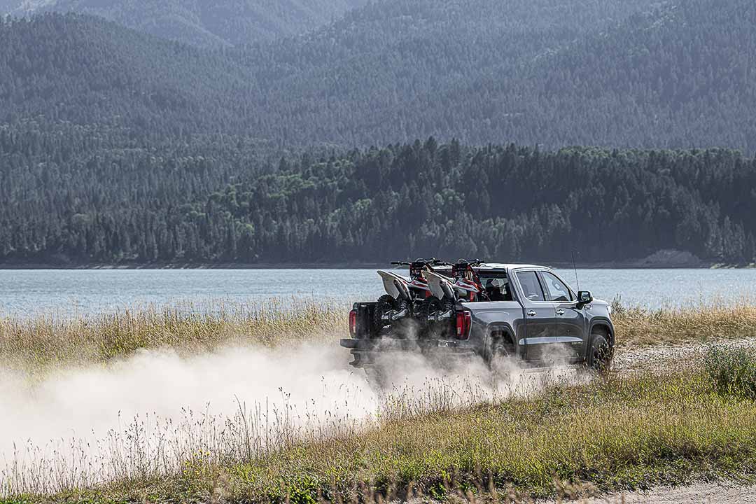 vue trois quart arrière du GMC Sierra 1500 2021 roulant sur un sentier proche d'une étendue d'eau