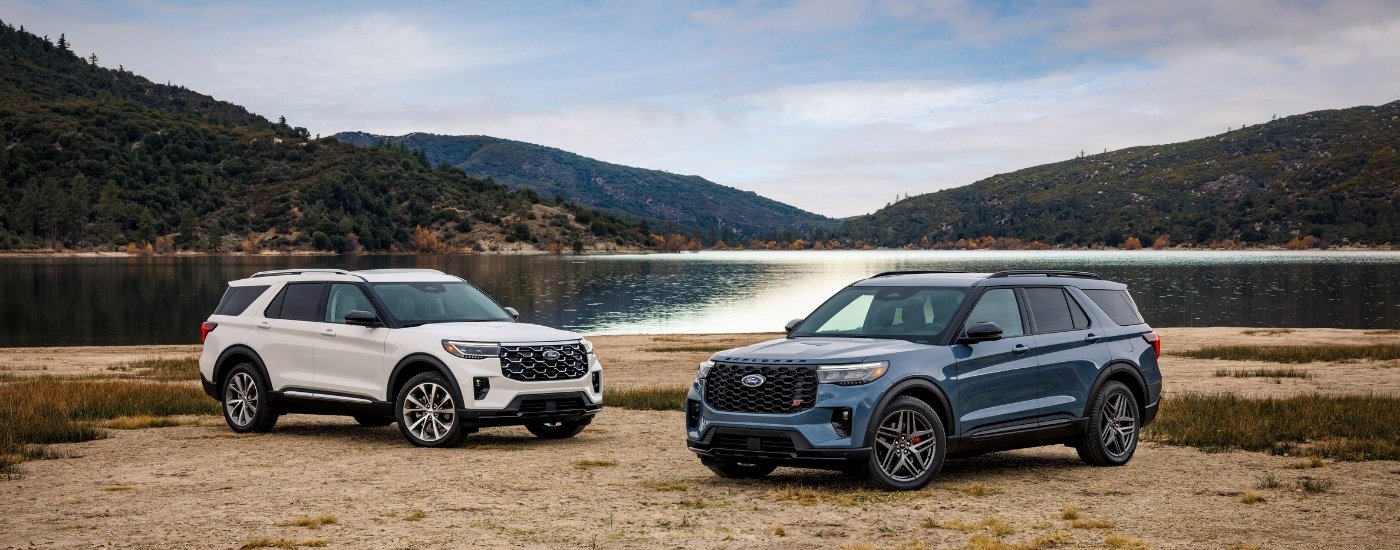 A white and a blue 2025 Ford Explorer for sale near Forest parked off-road.