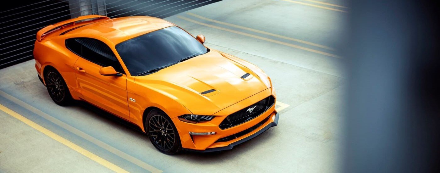 used%20car%20dealer%20-%202018%20Ford%20Mustang%20GT%20-%20Parked.jpg An orange 2018 Ford Mustang GT parked on a parking spot.