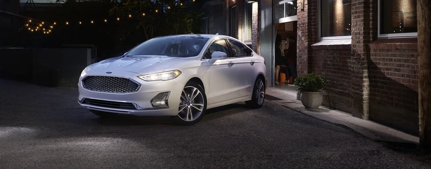 used%20car%20dealer%20-%202020%20Ford%20Fusion%20%20-%20Night%20(1).jpg A white 2020 Ford Fusion parked near a brick building.