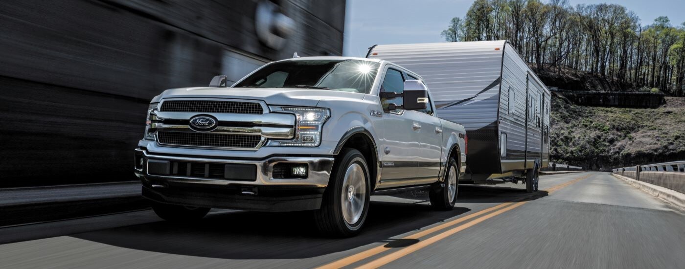 used%20car%20dealer%20-%202018%20Ford%20F-150%20-%20White.jpg A white 2018 Ford F-150 towing a trailer on a highway.