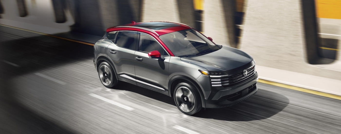 Black 2025 Nissan Kicks SR for sale near Troy driving under a bridge.