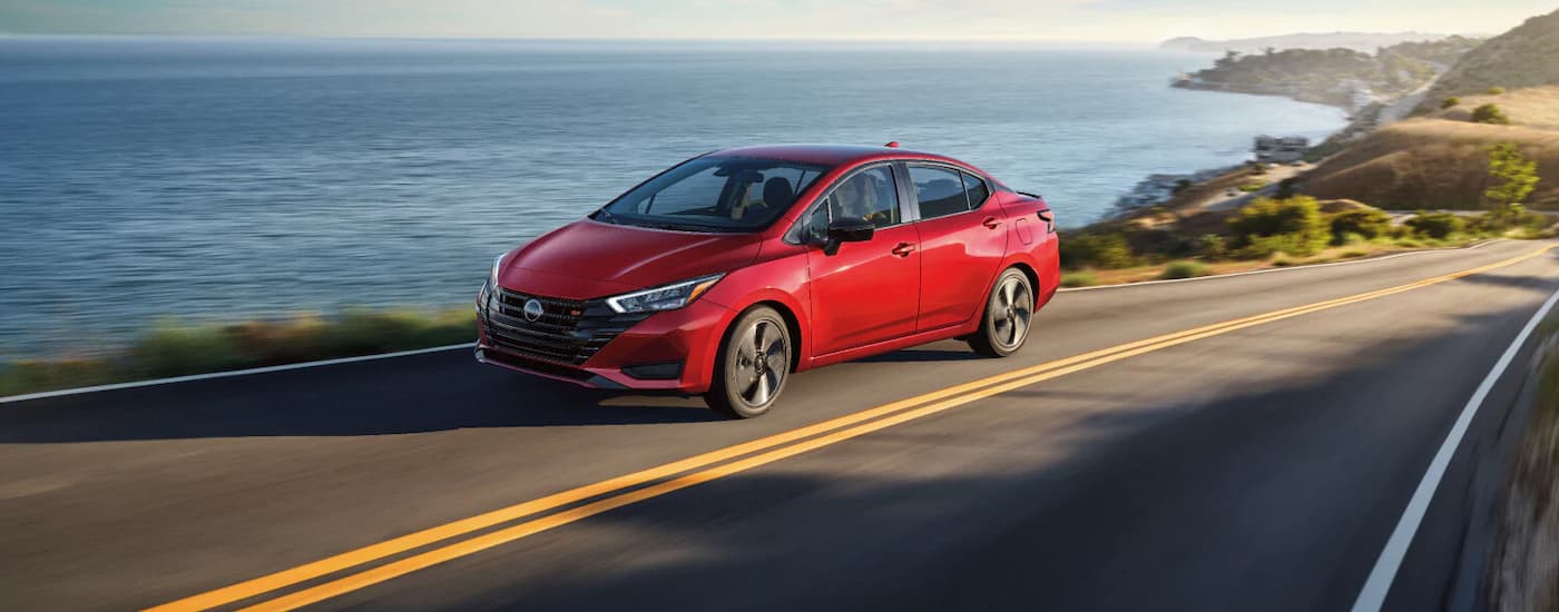 Nissan%20Versa%20for%20Sale%20Near%20Troy%20-%202026%20Nissan%20Versa%20Driving.jpg Red 2025 Nissan Versa driving on a road near a lake