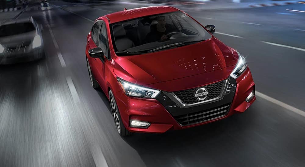 Used%20Nissan%20for%20Sale%20-%202021%20Nissan%20Versa%20-%20Red.jpg A red 2021 Nissan Versa driving down a road from a dealer with a used Nissan for sale.