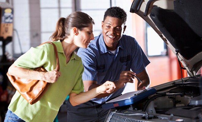 Ford Technician and driver looking at clipboard under car hood