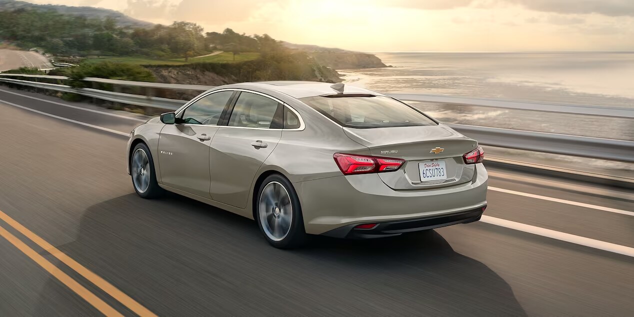 A Chevrolet Malibu driving down a mountain road with a sunset in the distance.