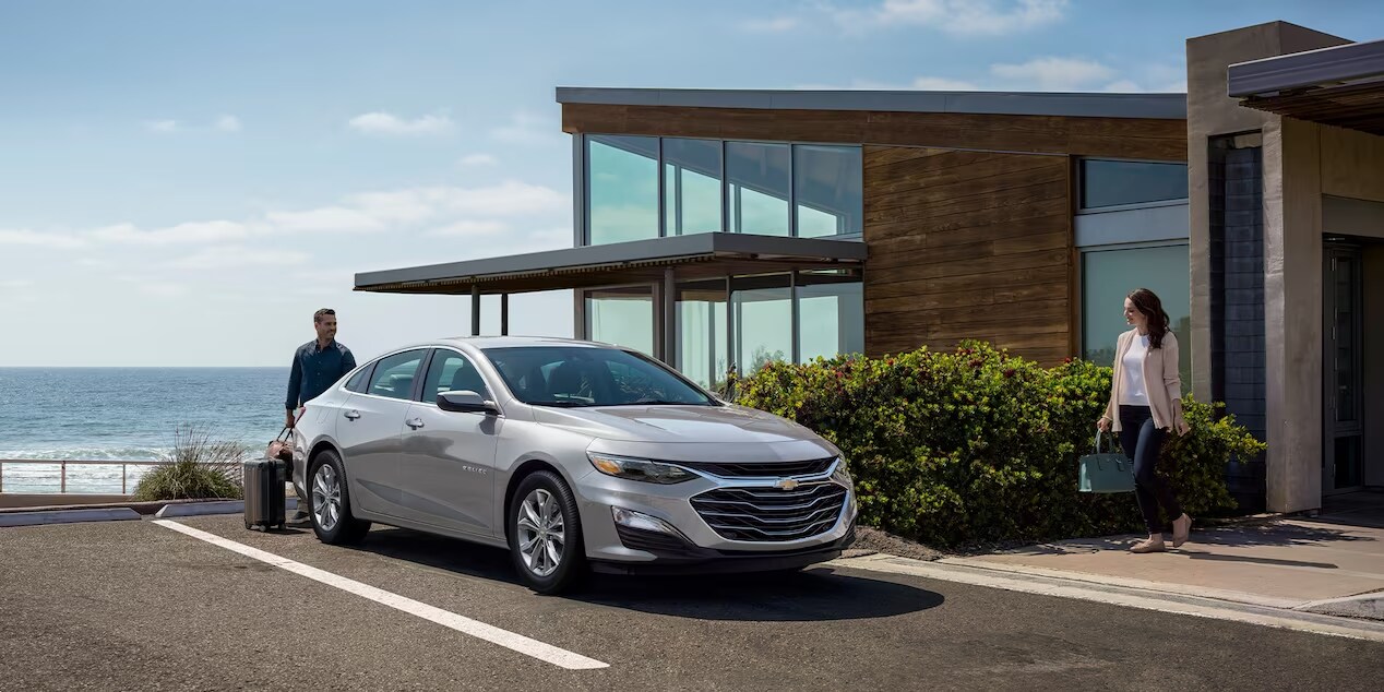 A modern 2024 Chevrolet Malibu parked in front of a suburban home.