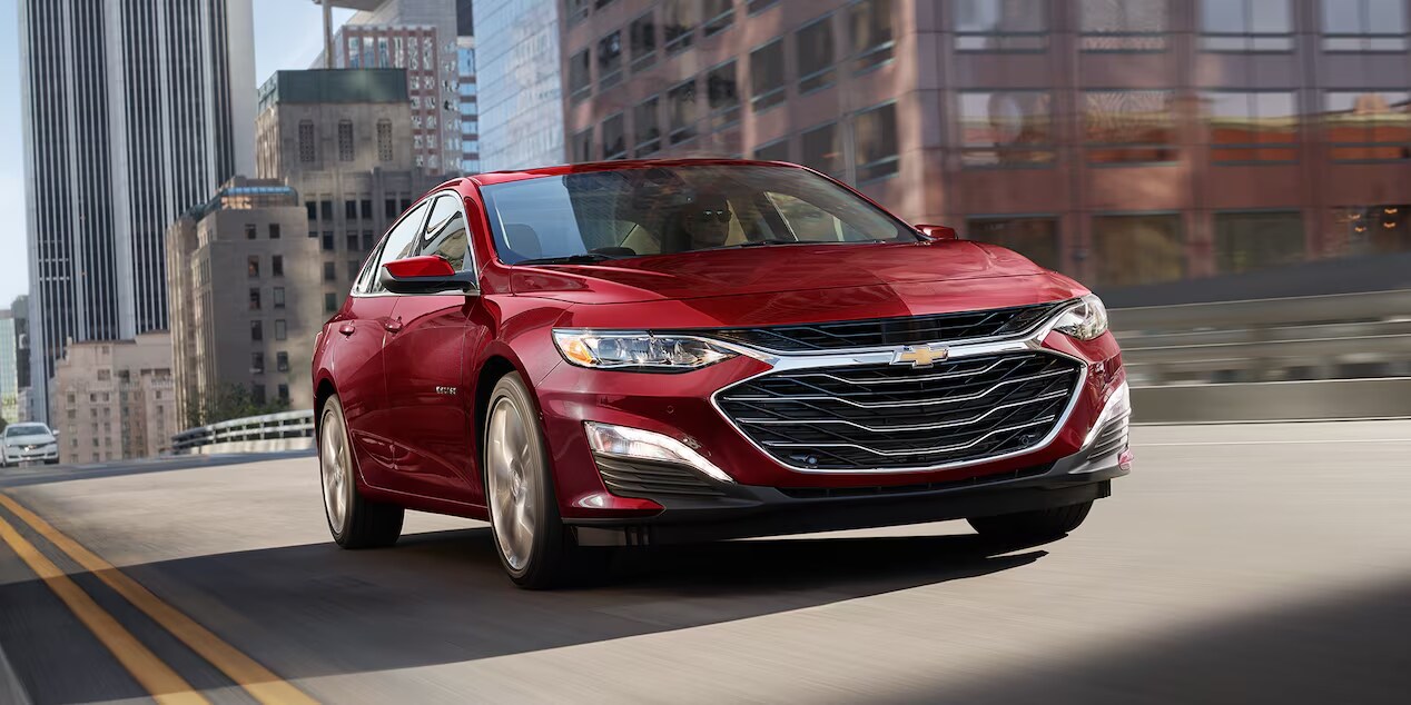 A red Chevrolet Malibu driving down a urban city street.
