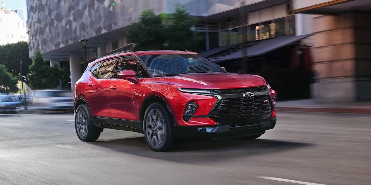 2024 Chevrolet Blazer driving in a city, highlighting its sleek exterior design and vibrant red color.