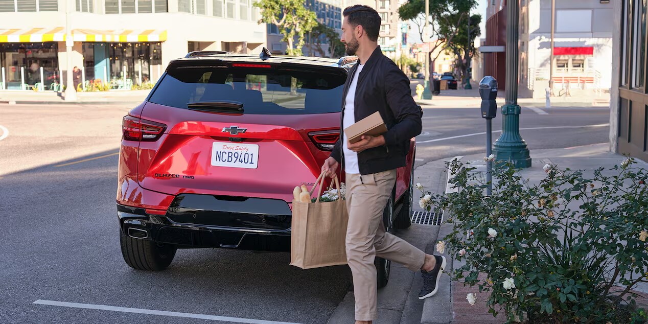 2024 Chevrolet Blazer parked on a city street with a man carrying groceries, showcasing the rear view and modern design of the vehicle.