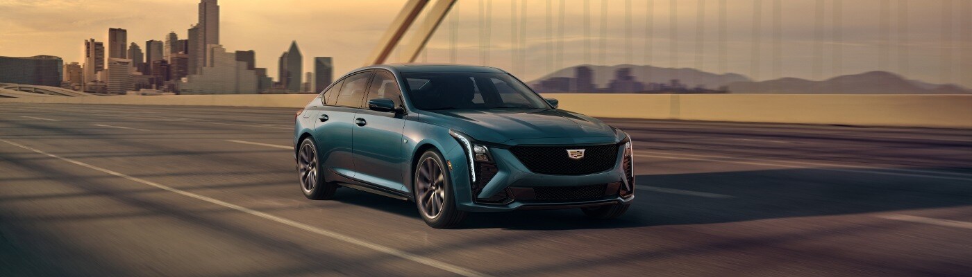 Dark Blue CADILLAC CT5 SUV driving down a narrow dark road at sunset new CADILLAC XT6