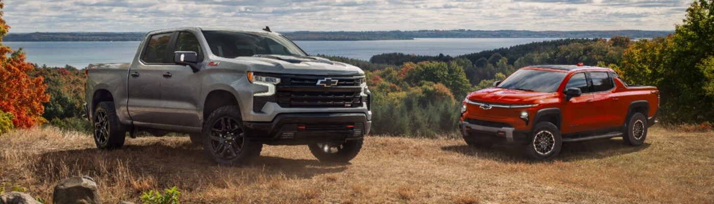Chevy EV Truck Lineup Chevrolet Silverado 1500 EVs parked side by side in front of a lake surrounded by trees