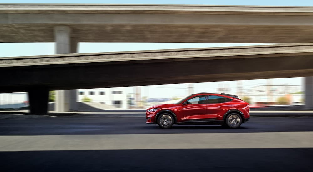 New Ford Dealership - 2022 Ford Mustang Mach-E Premium - Bridge.jpg A red 2022 Ford Mustang Mach-E Premium is shown from the side driving past a bride on its way to a new Ford dealersip.