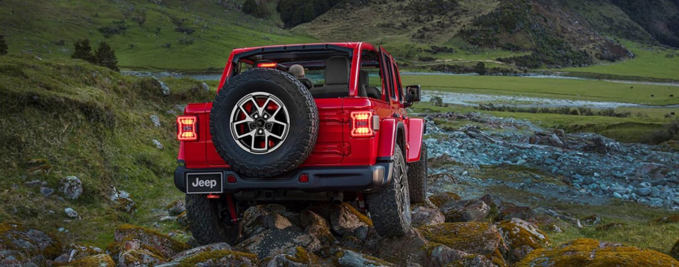 Rear of a red 2026 Jeep Wrangler driving off-road.