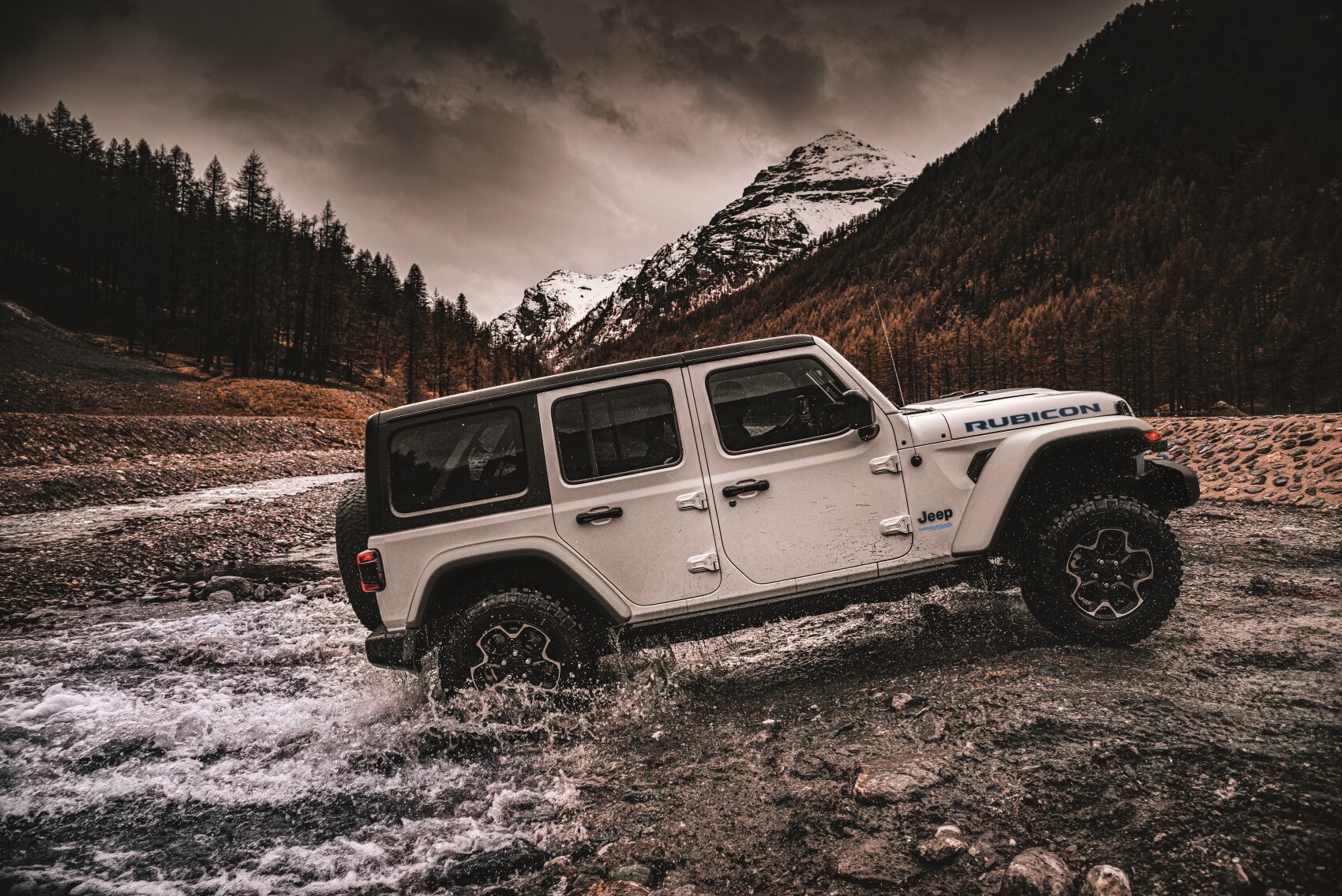 Jeep Wrangler 4xe Rubicon driving through river and dirt road with mountains in the background