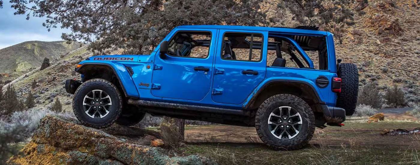A blue 2026 Jeep Wrangler Rubicon shown from the side parked on a cliff.