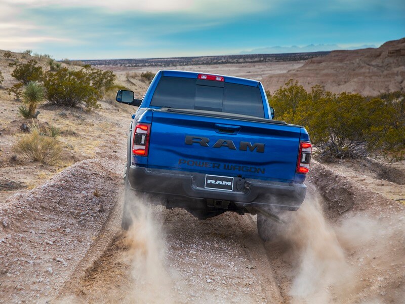 Back view of Ram 1500 truck driving through sand to the beach kicking up dirt behind it