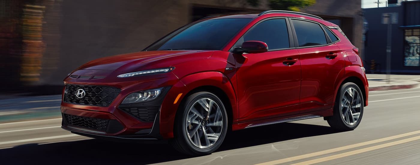 A red 2022 Hyundai Kona driving down a paved road.