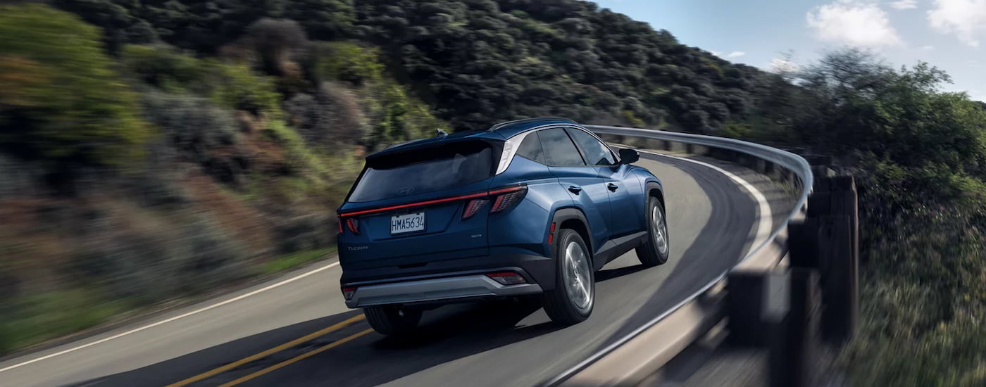 Rear of a blue 2026 Hyundai Tucson driving up a hill.
