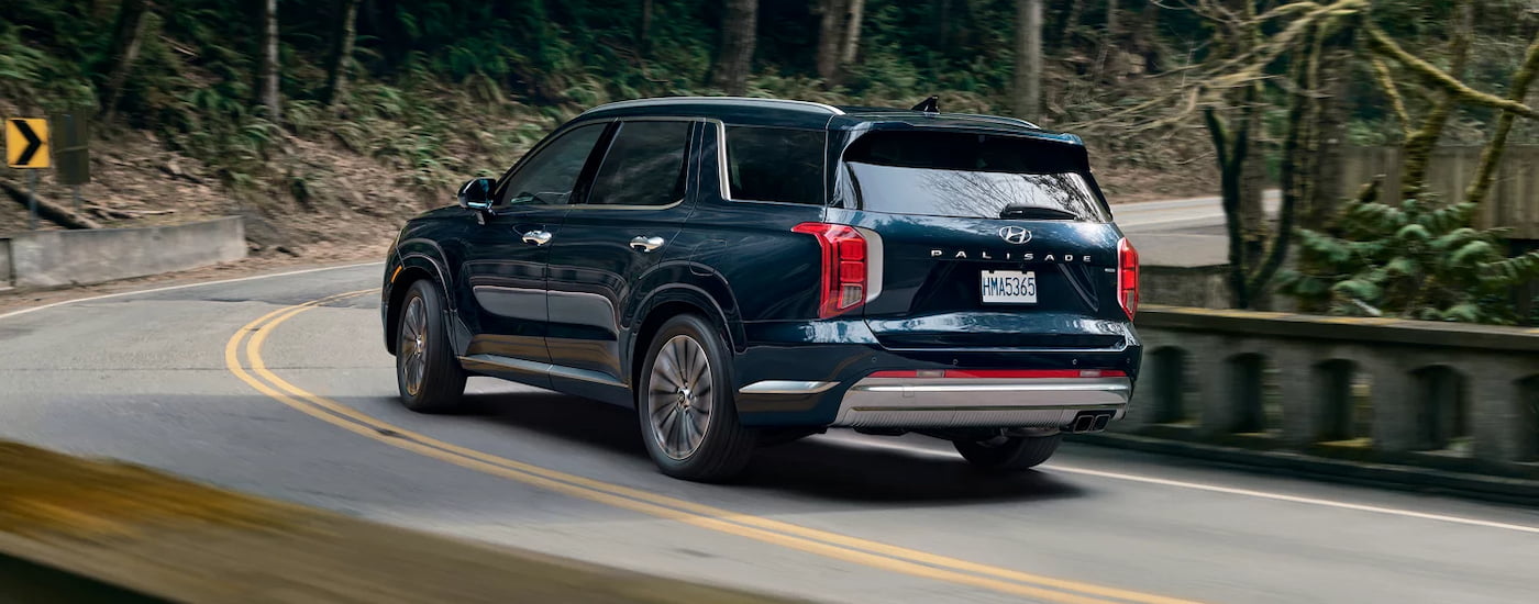 Rear of a green 2026 Hyundai Palisade driving around a bend.