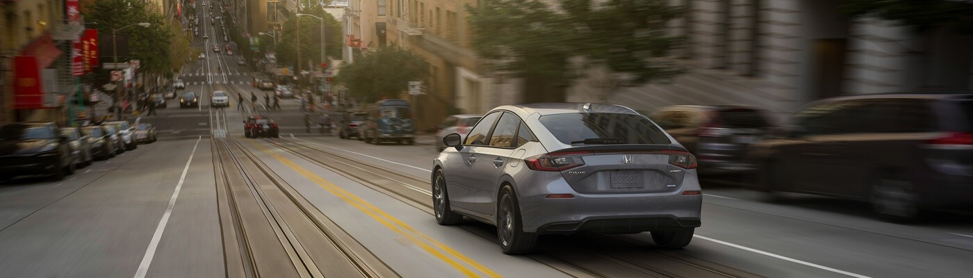 Honda Civic Hatchback Grey Civic Hatchback Sport Touring Hybrid driving down a hill in the city