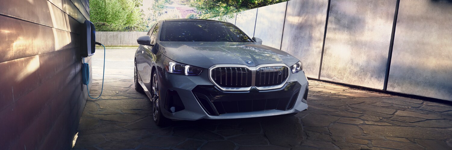 new BMW i5 silver BMW i5 electric sedan plugged in and charging while parked in a driveway