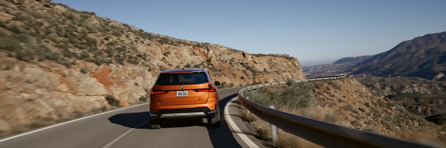 orange BMW X1 SUV driving down a mountain road new BMW X1