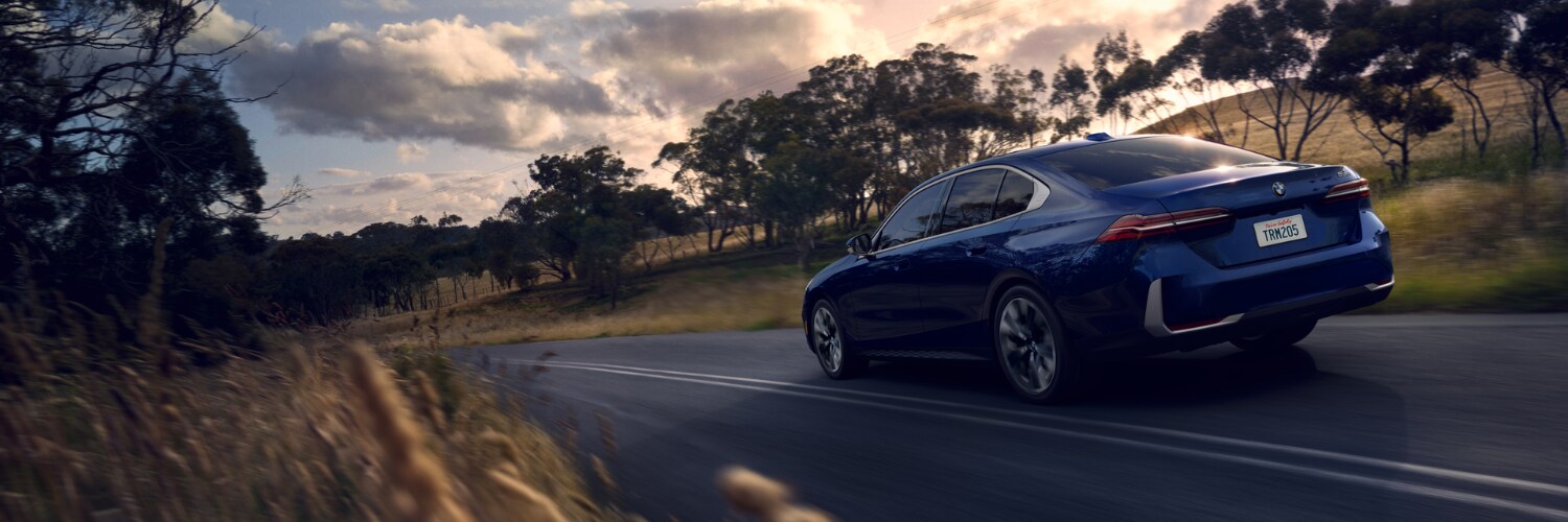 new BMW 5 Series sedan dark blue BMW 5 Series sedan seen from behind as it drive on a road through a field with trees