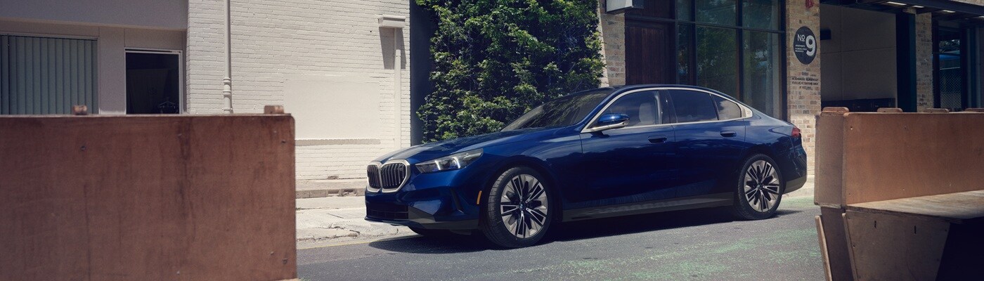 BMW 5 Series Sedan Dark Blue BMW 5 Series parked in front of a cafe in a city