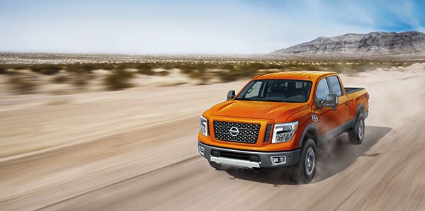 An orange 2019 Nissan Titan XD driving down a dusty road.